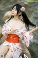 A woman in a pink kimono sitting on a rock by the water.