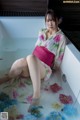 A woman sitting in a bathtub filled with water and flowers.