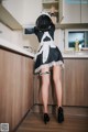 A woman in a maid outfit is standing in a kitchen.