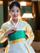 A woman in a yellow and green hanbok poses for a picture.